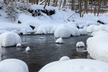 Yoğun karla kaplı büyük kayalar akan bir derede oturur ve yumuşak, yuvarlak şekilli eşsiz bir kış manzarası yaratır..