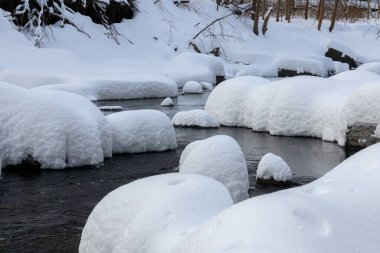 Yoğun karla kaplı büyük kayalar akan bir derede oturur ve yumuşak, yuvarlak şekilli eşsiz bir kış manzarası yaratır..