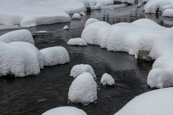 Yoğun karla kaplı büyük kayalar akan bir derede oturur ve yumuşak, yuvarlak şekilli eşsiz bir kış manzarası yaratır..