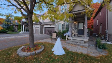 Bir ön bahçede büyük bir evin önünde gösterişli cadılar bayramı süslemeleri vardır..