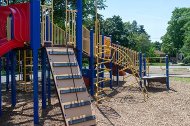 Güneşli bir gün sahnesi. Slaytlar, merdivenler ve yerde ağaçlar ve odun parçalarıyla çevrili tırmanma sahaları..