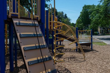 Güneşli bir gün sahnesi. Slaytlar, merdivenler ve yerde ağaçlar ve odun parçalarıyla çevrili tırmanma sahaları..