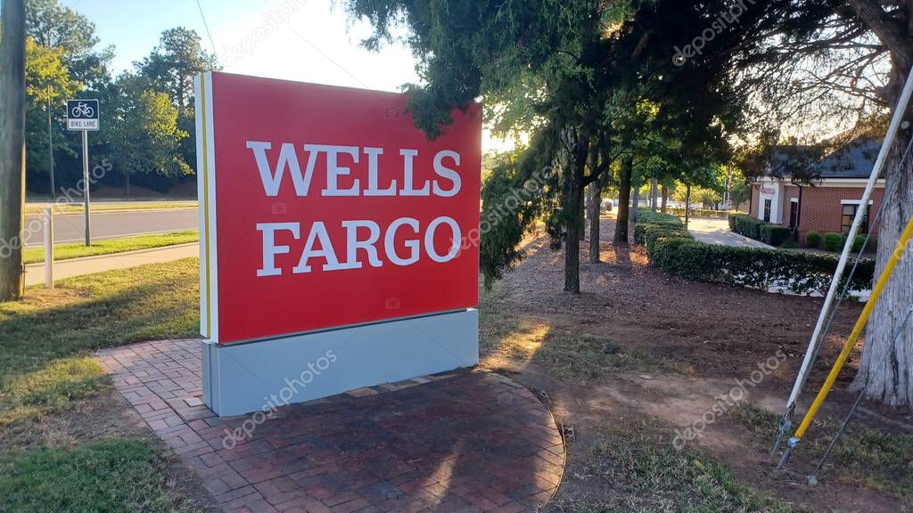 Charlotte, NC, USA - October 10, 2025: Large red Wells Fargo sign stands near a road and trees on a sunny autumn afternoon