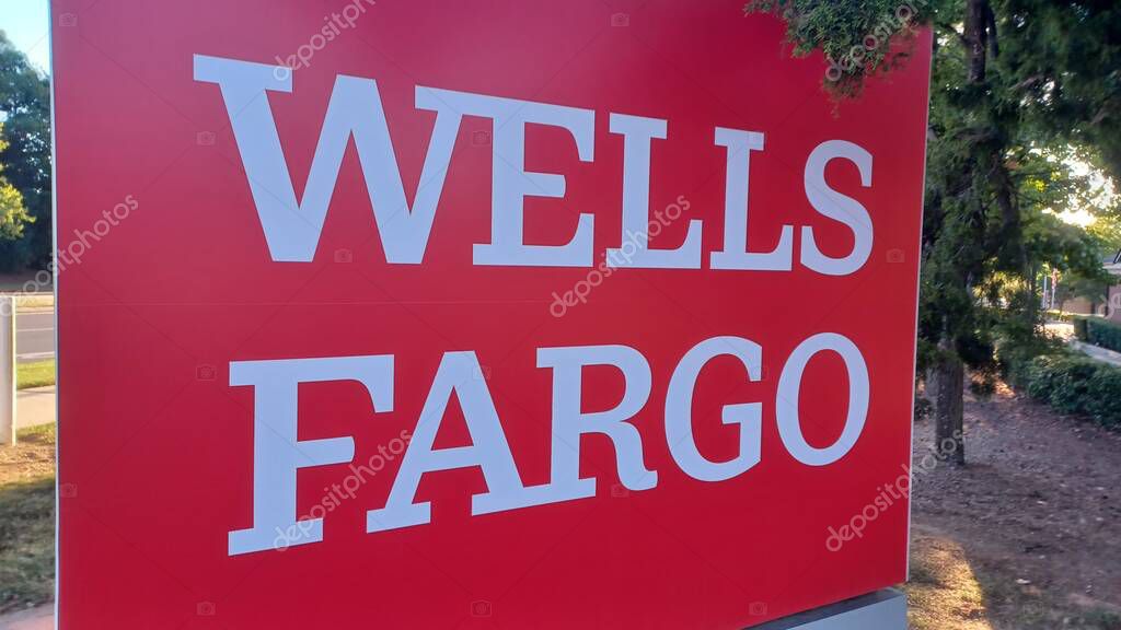 Charlotte, NC, USA - October 10, 2025: Large red Wells Fargo sign stands near a road and trees on a sunny autumn afternoon
