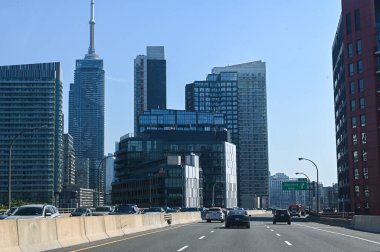 Toronto, Kanada - 30 Eylül 2025: CN Kulesi ve açık mavi gökdelenler altında görünen modern gökdelenlerle şehir merkezindeki bir otoyolda arabalar sürüyor.