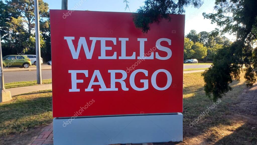 Charlotte, NC, USA - October 10, 2025: Large red Wells Fargo sign stands near a road and trees on a sunny autumn afternoon