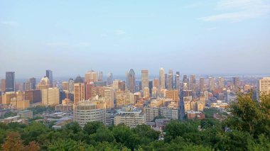 Montreal, Quebec, Kanada - 7 Ağustos 2025: Yüksek açılı bir manzara yeşil ağaçların üzerinde yükselen gökdelenlerin yoğun bir şehir siluetini gösteriyor.