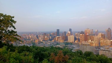 Montreal, Quebec, Kanada - 7 Ağustos 2025: Yüksek açılı bir manzara yeşil ağaçların üzerinde yükselen gökdelenlerin yoğun bir şehir siluetini gösteriyor.