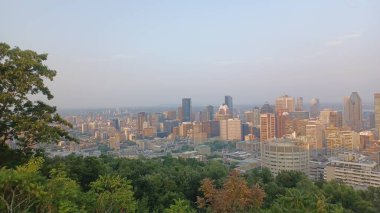 Montreal, Quebec, Kanada - 7 Ağustos 2025: Yüksek açılı bir manzara yeşil ağaçların üzerinde yükselen gökdelenlerin yoğun bir şehir siluetini gösteriyor.
