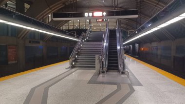 Toronto, ON, Kanada - 31 Ekim 2025: Toronto Transit Komisyonu 'nun (TTC) metro istasyonunun boş bir metro platformu, üst kata çıkan uzun bir yürüyen merdiven ve merdiven ve mesafeye giden bir tren ile birlikte..