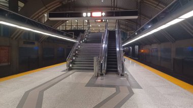 Toronto, ON, Kanada - 31 Ekim 2025: Toronto Transit Komisyonu 'nun (TTC) metro istasyonunun boş bir metro platformu, üst kata çıkan uzun bir yürüyen merdiven ve merdiven ve mesafeye giden bir tren ile birlikte..