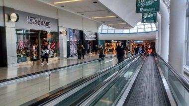 Toronto, ON, Kanada - 12 Ekim 2025: Yolcular geniş pencereli modern bir havaalanı terminali içinde hareket halindeki bir geçitte seyahat ediyorlar.