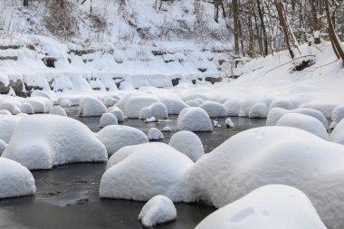 Yoğun karla kaplı büyük kayalar akan bir derede oturur ve yumuşak, yuvarlak şekilli eşsiz bir kış manzarası yaratır..