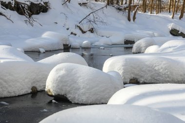 Yoğun karla kaplı büyük kayalar akan bir derede oturur ve yumuşak, yuvarlak şekilli eşsiz bir kış manzarası yaratır..