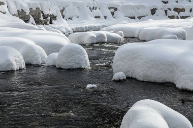 Yoğun karla kaplı büyük kayalar akan bir derede oturur ve yumuşak, yuvarlak şekilli eşsiz bir kış manzarası yaratır..