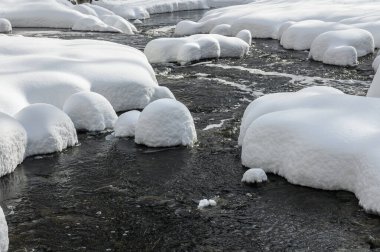 Yoğun karla kaplı büyük kayalar akan bir derede oturur ve yumuşak, yuvarlak şekilli eşsiz bir kış manzarası yaratır..