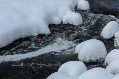 Yoğun karla kaplı büyük kayalar akan bir derede oturur ve yumuşak, yuvarlak şekilli eşsiz bir kış manzarası yaratır..