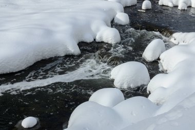 Yoğun karla kaplı büyük kayalar akan bir derede oturur ve yumuşak, yuvarlak şekilli eşsiz bir kış manzarası yaratır..