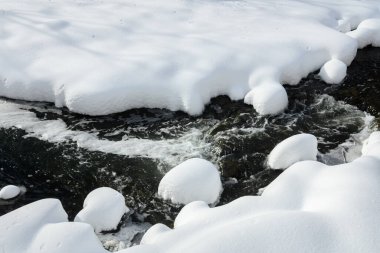 Yoğun karla kaplı büyük kayalar akan bir derede oturur ve yumuşak, yuvarlak şekilli eşsiz bir kış manzarası yaratır..