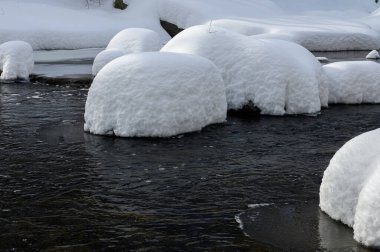 Yoğun karla kaplı büyük kayalar akan bir derede oturur ve yumuşak, yuvarlak şekilli eşsiz bir kış manzarası yaratır..