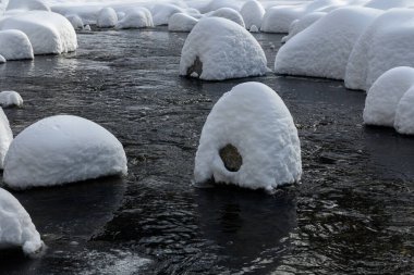 Yoğun karla kaplı büyük kayalar akan bir derede oturur ve yumuşak, yuvarlak şekilli eşsiz bir kış manzarası yaratır..