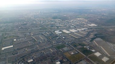 Dallas, TX, ABD - 9 Temmuz 2025 - Geniş bir hava manzarası ticari ve endüstriyel binaların yoğun kentsel manzarasını ve uzaktaki puslu bir şehir siluetine doğru uzanan büyük otoyolları gösteriyor.