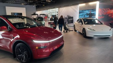 Toronto, ON, Kanada - 8 Kasım 2025: Kırmızı bir Tesla Model Y ve beyaz bir Tesla aracı büyük camlı ve kırmızı duvar aksanlı modern bir Tesla galerisinde sergilenmektedir.