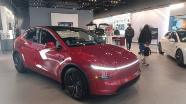 Toronto, ON, Kanada - 8 Kasım 2025: Kırmızı bir Tesla Model Y ve beyaz bir Tesla aracı büyük camlı ve kırmızı duvar aksanlı modern bir Tesla galerisinde sergilenmektedir.