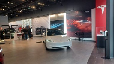 Toronto, ON, Kanada - 8 Kasım 2025: Kırmızı bir Tesla Model Y ve beyaz bir Tesla aracı büyük camlı ve kırmızı duvar aksanlı modern bir Tesla galerisinde sergilenmektedir.
