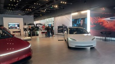Toronto, ON, Kanada - 8 Kasım 2025: Kırmızı bir Tesla Model Y ve beyaz bir Tesla aracı büyük camlı ve kırmızı duvar aksanlı modern bir Tesla galerisinde sergilenmektedir.