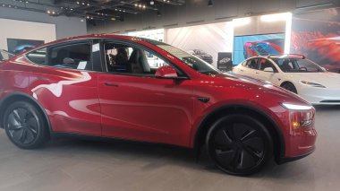 Toronto, ON, Kanada - 8 Kasım 2025: Kırmızı bir Tesla Model Y ve beyaz bir Tesla aracı büyük camlı ve kırmızı duvar aksanlı modern bir Tesla galerisinde sergilenmektedir.