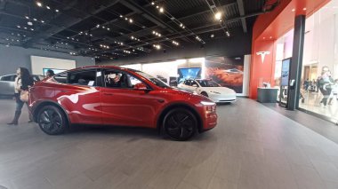 Toronto, ON, Kanada - 8 Kasım 2025: Kırmızı bir Tesla Model Y ve beyaz bir Tesla aracı büyük camlı ve kırmızı duvar aksanlı modern bir Tesla galerisinde sergilenmektedir.