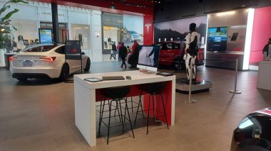 Toronto, ON, Kanada - 8 Kasım 2025: Kırmızı bir Tesla Model Y ve beyaz bir Tesla aracı büyük camlı ve kırmızı duvar aksanlı modern bir Tesla galerisinde sergilenmektedir.