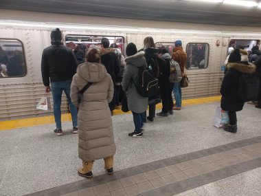 Toronto, ON, Kanada - 6 Kasım 2025: Banliyö treni kalabalık bir metro istasyonunda, kışlık giysiler giyerek ve kentsel ulaşım araçlarında çanta taşıyarak bekliyor.