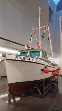 Ottawa, ON, Kanada - 11 Ağustos 2025 - Renkli bayraklarla süslenmiş tarihi bir balıkçı teknesi modern bir müze salonunda sergilenmektedir..