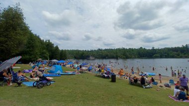 Rockwood, ON, Kanada - 19 Ağustos 2025: Büyük bir kalabalık bulutlu bir yaz gününde çimlerin üzerinde rahatlar ve gölde yüzer..