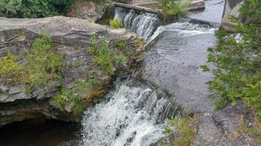 Küçük, köpüklü bir şelale engebeli gri kireçtaşı kayaları ve yeşil bitki örtüsü üzerinde doğal bir ortamda çağlıyor..