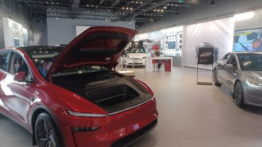 Toronto, ON, Kanada - 25 Kasım 2025: Biri kırmızı diğeri gümüş olmak üzere iki modern Tesla elektrikli otomobili, markalı duvar resimleri ve dijital ekran ile çağdaş bir otomobil galerisinde sergilenmektedir..