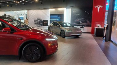 Toronto, ON, Kanada - 25 Kasım 2025: Biri kırmızı diğeri gümüş olmak üzere iki modern Tesla elektrikli otomobili, markalı duvar resimleri ve dijital ekran ile çağdaş bir otomobil galerisinde sergilenmektedir..
