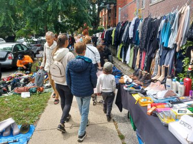 Toronto, ON, Canada - October 5, 2025: People shop at an outdoor flea market as various items of clothing are hung on a fence for display and shopping in an urban setting.