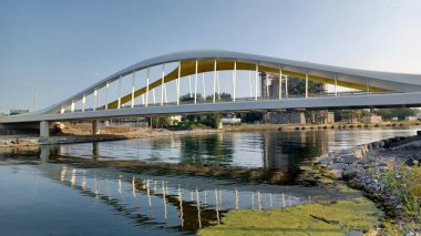 Toronto, ON, Kanada - 6 Temmuz 2025: Sarı kirişli modern bir kemerli köprü, açık ve güneşli bir günde yansımalı bir su kanalı boyunca uzanır.