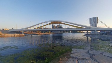 Toronto, ON, Kanada - 6 Temmuz 2025: Sarı kirişli modern bir kemerli köprü, açık ve güneşli bir günde yansımalı bir su kanalı boyunca uzanır.