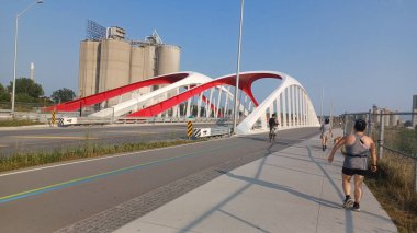 Toronto, ON, Kanada - 6 Temmuz 2025: Sarı kirişli modern bir kemerli köprü, açık ve güneşli bir günde yansımalı bir su kanalı boyunca uzanır.