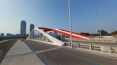 Toronto, ON, Kanada - 6 Temmuz 2025: Sarı kirişli modern bir kemerli köprü, açık ve güneşli bir günde yansımalı bir su kanalı boyunca uzanır.