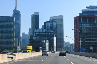Toronto, Kanada - 30 Eylül 2025: CN Kulesi ve açık mavi gökdelenler altında görünen modern gökdelenlerle şehir merkezindeki bir otoyolda arabalar sürüyor.