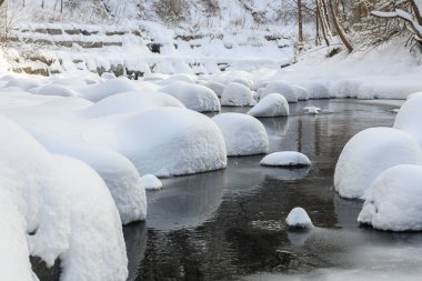 Yoğun karla kaplı büyük kayalar akan bir derede oturur ve yumuşak, yuvarlak şekilli eşsiz bir kış manzarası yaratır..
