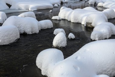 Yoğun karla kaplı büyük kayalar akan bir derede oturur ve yumuşak, yuvarlak şekilli eşsiz bir kış manzarası yaratır..