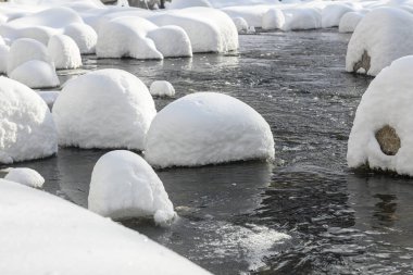 Yoğun karla kaplı büyük kayalar akan bir derede oturur ve yumuşak, yuvarlak şekilli eşsiz bir kış manzarası yaratır..
