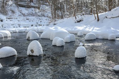 Yoğun karla kaplı büyük kayalar akan bir derede oturur ve yumuşak, yuvarlak şekilli eşsiz bir kış manzarası yaratır..