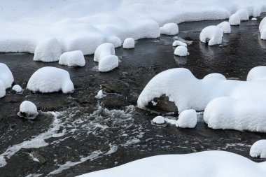Yoğun karla kaplı büyük kayalar akan bir derede oturur ve yumuşak, yuvarlak şekilli eşsiz bir kış manzarası yaratır..